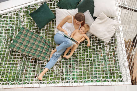 Young mother hugging her baby on mesh hammockの写真素材