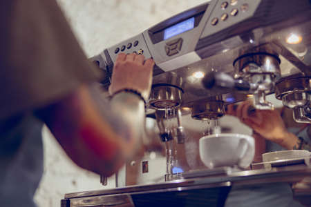 Young woman barista using coffee machine in cafeteriaの写真素材