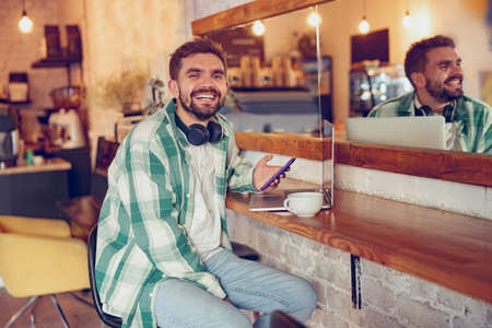 Cheerful man using smartphone and laptop in cafeの写真素材
