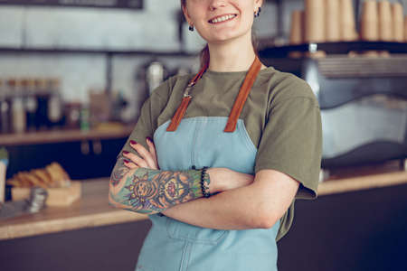 Cheerful female barista in apron standing in coffee shopの写真素材