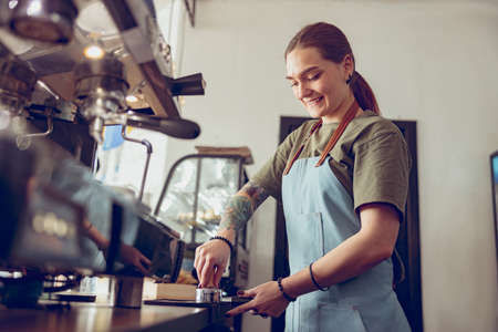 Cheerful woman barista making coffee in cafeteriaの写真素材