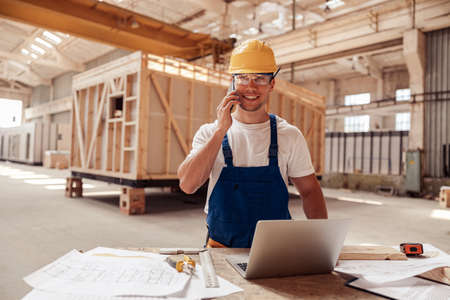 Cheerful male builder talking on cellphone at work