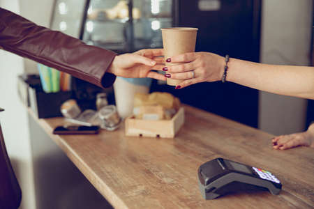 Female barista hand giving cup of coffee to woman