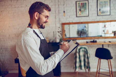 Cheerful bearded man writing on clipboard in cafeの写真素材