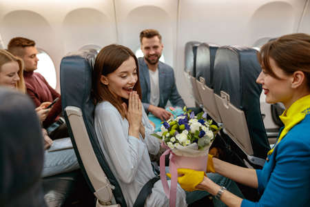 Flight attendant giving flowers to woman in airplaneの写真素材