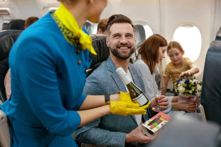 Flight attendant giving champagne to man in airplaneの写真素材