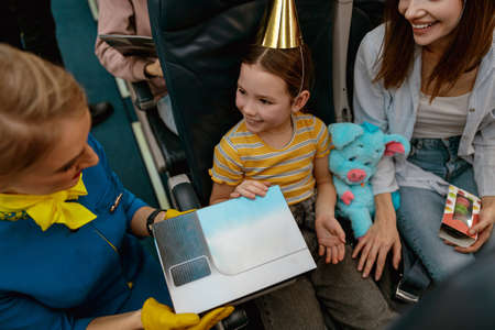 Flight attendant giving birthday present to little girl in airplaneの写真素材