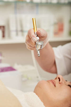 Close up of doctor cosmetologist hand holding oxygen mesotherapy device while female client waiting...