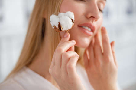 Young woman holding cotton plant near faceの写真素材
