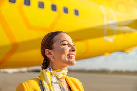 Cheerful woman stewardess standing near aircraft at airfieldの写真素材