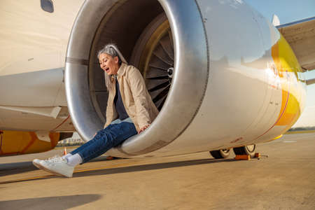 Joyful woman sitting in airplane engine at airport