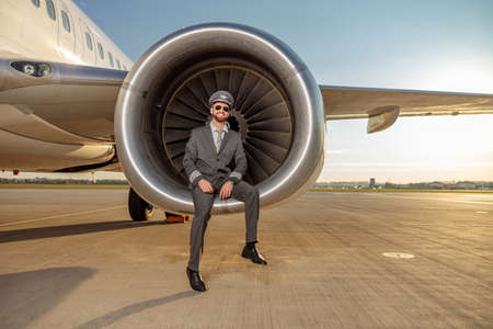 Cheerful male pilot sitting in airplane engine at airport