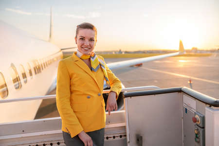 Cheerful female stewardess standing near airplane at airportの写真素材