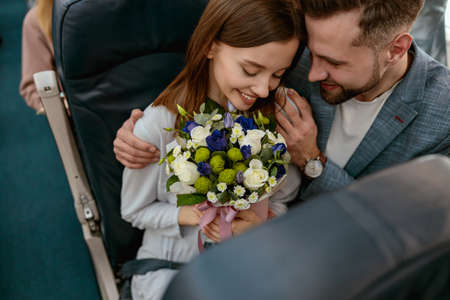 Happy man hugging woman with flowers in airplaneの写真素材