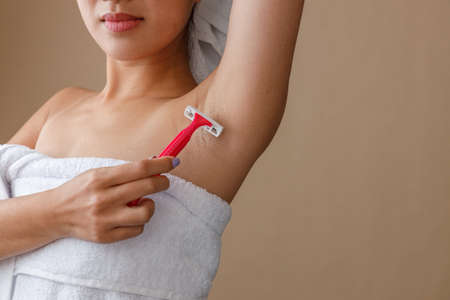 Young woman shaving armpit with razor after showerの写真素材