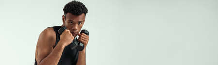 Perfect body. Muscular young african man exercising with dumbbells while standing against grey backgroundの写真素材