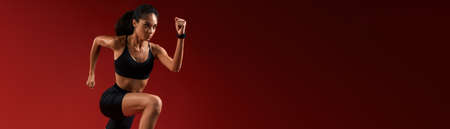 Higher and higher. Full length of young athlete woman in sports clothing jumping against red...