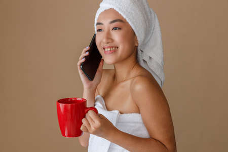 Cheerful Asian woman talking on cellphone after showerの写真素材