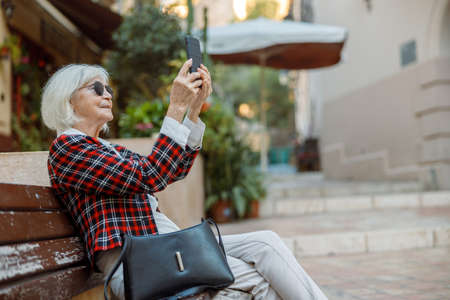Charming elderly woman relaxing on bench outdoorsの写真素材