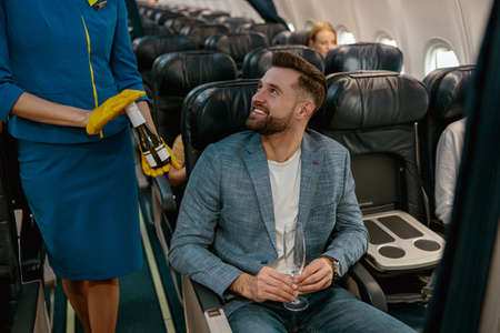 Stewardess offering champagne to cheerful man in airplane