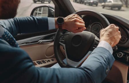 Confident male entrepreneur wearing suit driving a car while looking at his watch
