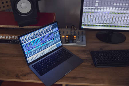 Top view of switched on laptop and monitor screen on table in sound engineer room in a broadcasting and recording studioの写真素材