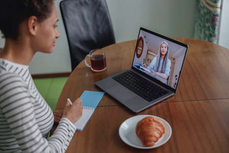 Close up shot of pretty young woman studying having online video lesson sitting in kitchen