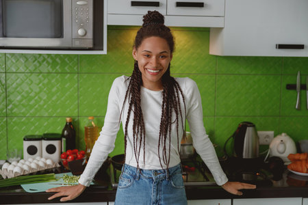Portrait of cheerful young mixed-race woman smiling to camera standing in the kitchen