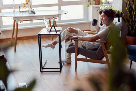 Smiling young guy listening to music with headphones and holding a cup of coffee