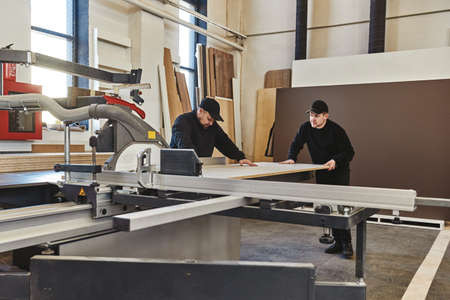 Sawing up of a wooden board on a sliding table saw. Woodworking and carpentry production. Furniture manufacture.の写真素材