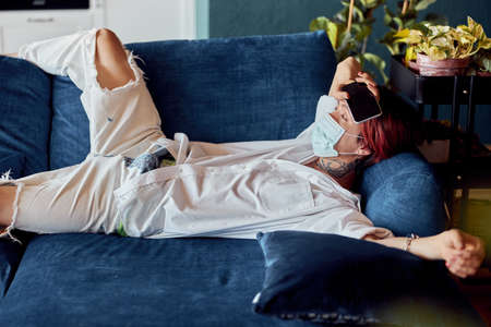 Asian man in medical mask enjoying rest on the sofa at flatの写真素材