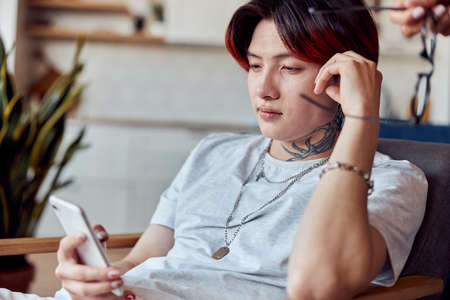 Asian guy sitting at his appartment while using smartphone