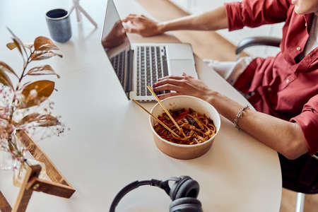 Young man typing on a laptop and going to eat noodles at home