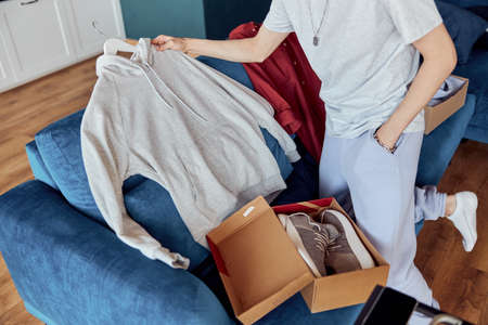 Young man unpacking online shopping at home while holding hoodieの写真素材