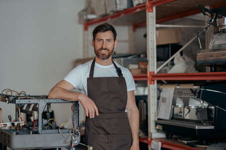 Portrait of repairman in uniform standing on workshop of coffee machines warehouse