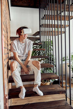 Young Asian man sitting on steps and wearing VR glasses