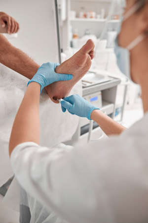 Woman grinds heel of man with modern machine at pedicure procedure in salonの写真素材