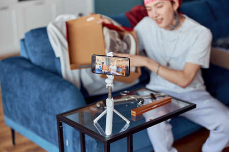 Smiling Asian guy using smartphone and taking live selling shoes online