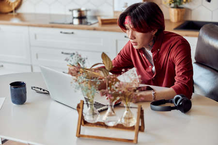 Asian guy eating noodles and working online at homeの写真素材