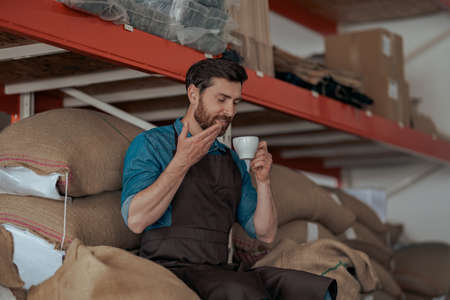 Business owner inhaling smell of fresh coffee sitting on warehouse of coffee factoryの写真素材