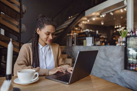 Confident young mixed race student, freelancer typing text on laptop keyboard while studying online in cafe interiorの写真素材