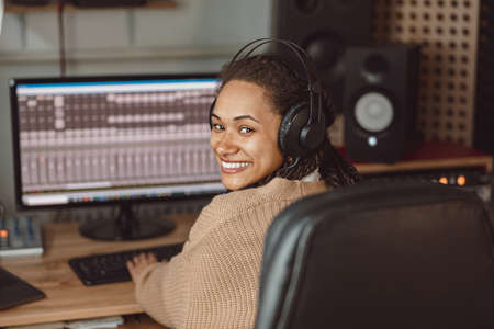 Cheerful African American young female musician, composer, sound engineer working in the music recording studioの写真素材