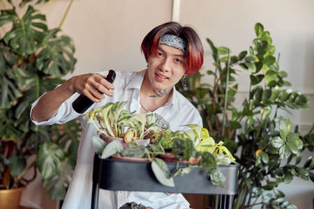 Smiling man taking care of plants and holding spray bottle at homeの写真素材