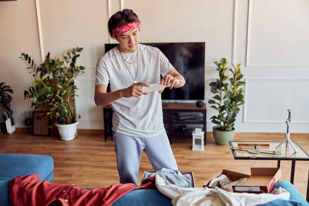 Smiling Asian guy taking photos of new purchases in the living room