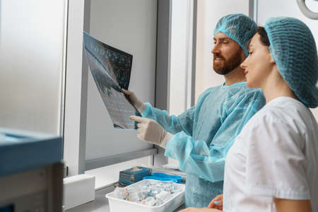 Doctor and nurse in uniform look and discuss an X-ray or MRI scan of the patient spineの写真素材