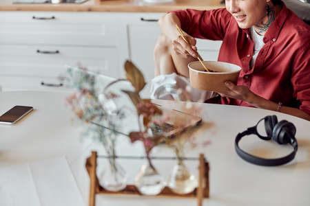 Smiling Asian guy eating hot instant noodle and work with laptop