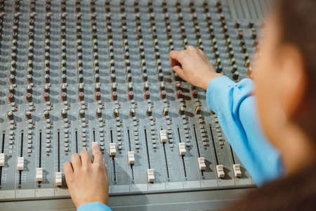 Rear view of audio engineer, producer working in music recording studio, using mixing board, software to create new songの写真素材