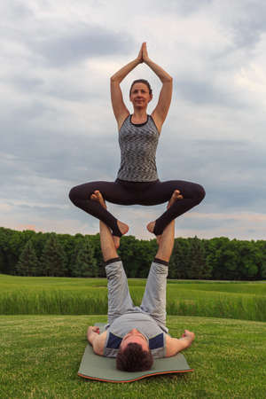 Young couple doing acro yoga in park. Man lying on grass and balancing woman in his feetの写真素材
