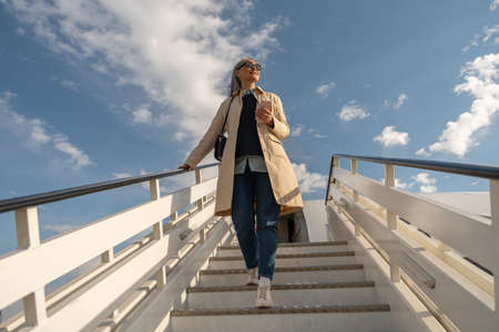 Happy woman passenger in sunglasses going down on aircraft stairs after landing at airport