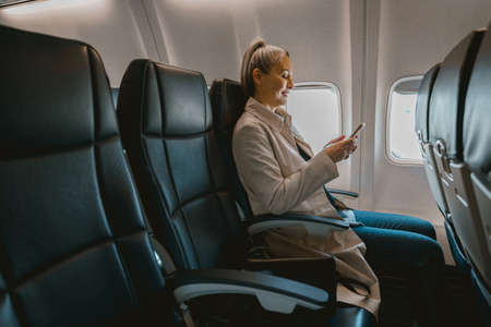 Beautiful Asian woman passenger sitting in the airplane and use phone during boarding